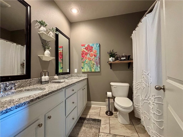 bathroom featuring double vanity, toilet, baseboards, and a sink