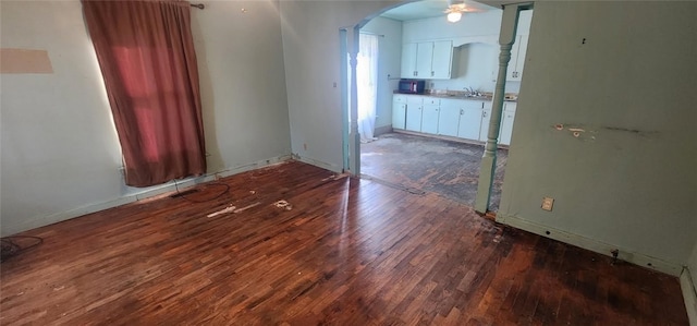 empty room with ceiling fan, baseboards, wood finished floors, arched walkways, and a sink