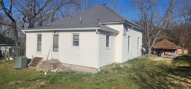 view of side of property featuring central air condition unit, entry steps, metal roof, and a yard