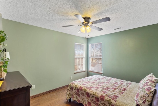 bedroom featuring visible vents, ceiling fan, baseboards, wood finished floors, and a textured ceiling