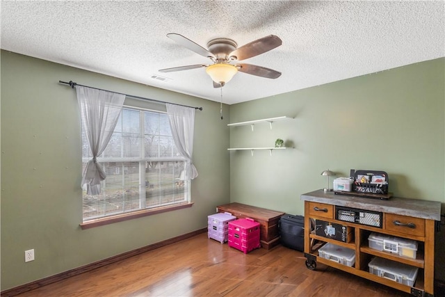 interior space with visible vents, a ceiling fan, a textured ceiling, wood finished floors, and baseboards