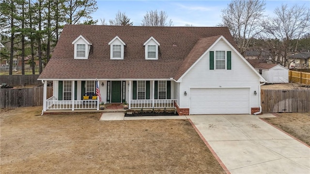 cape cod home featuring fence, an attached garage, covered porch, a shingled roof, and concrete driveway