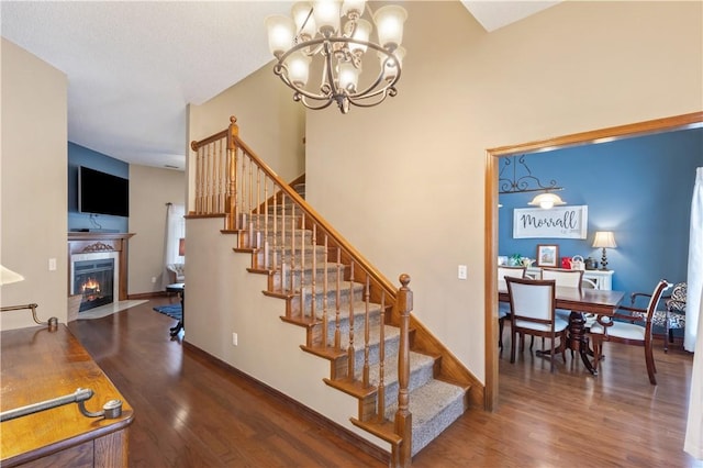 stairs featuring a chandelier, a fireplace with flush hearth, baseboards, and wood finished floors