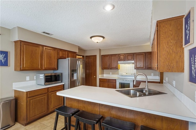 kitchen featuring visible vents, a peninsula, a sink, stainless steel appliances, and under cabinet range hood