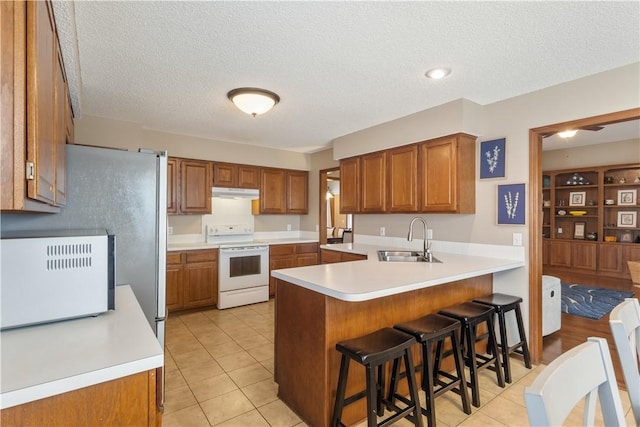 kitchen with a sink, a peninsula, brown cabinets, and white range with electric stovetop