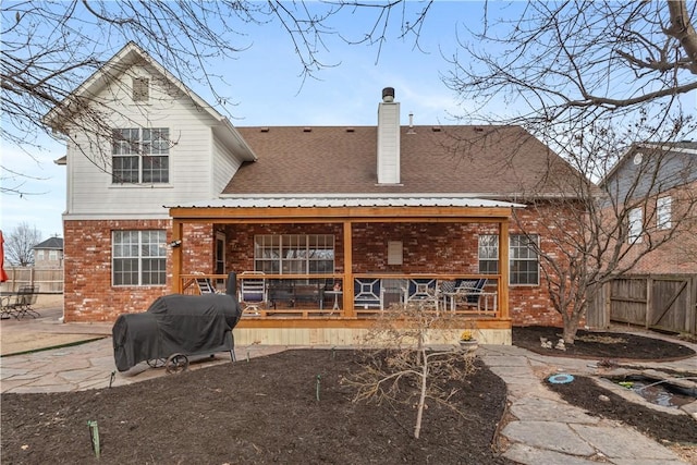 back of property with brick siding, a shingled roof, fence, a chimney, and a patio