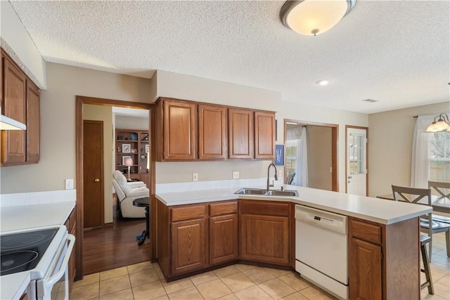 kitchen featuring white appliances, brown cabinetry, light countertops, and a sink