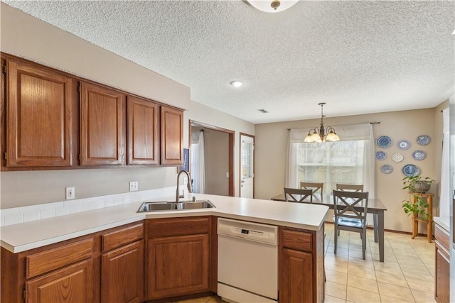 kitchen featuring brown cabinets, a peninsula, white dishwasher, a notable chandelier, and a sink