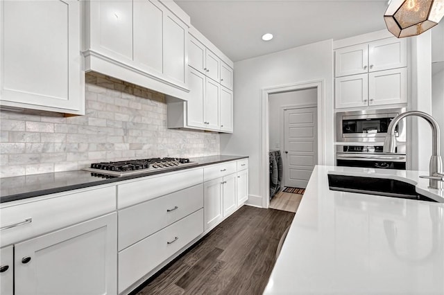 kitchen with washer / dryer, a sink, stainless steel appliances, dark wood-type flooring, and white cabinetry