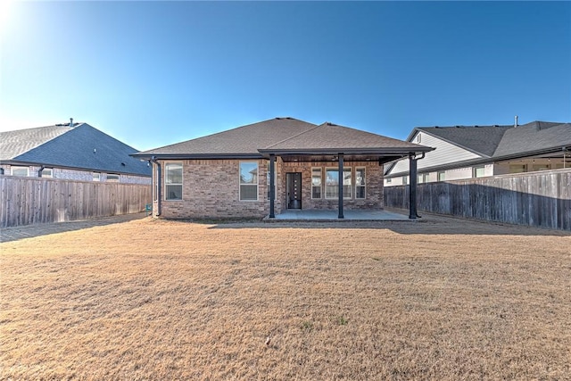 rear view of property with brick siding, a fenced backyard, a lawn, and a patio