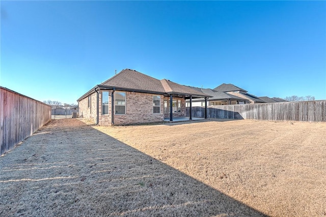 rear view of property featuring roof with shingles, a yard, a fenced backyard, a patio area, and brick siding