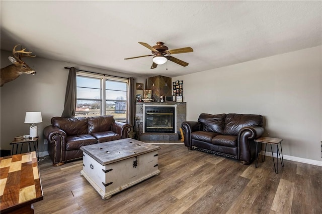 living room with a tile fireplace, baseboards, a ceiling fan, and wood finished floors