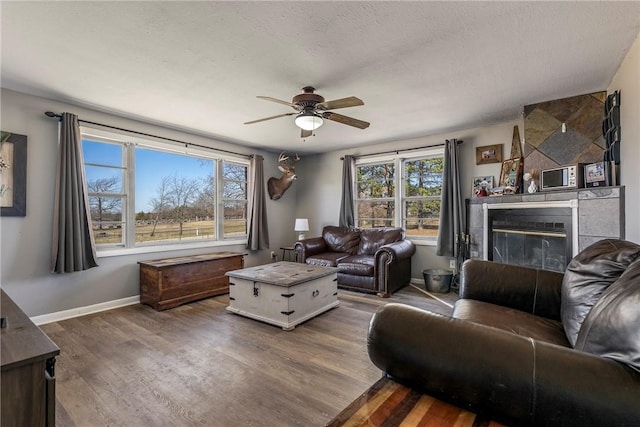 living area with a ceiling fan, a textured ceiling, a glass covered fireplace, dark wood-style floors, and baseboards