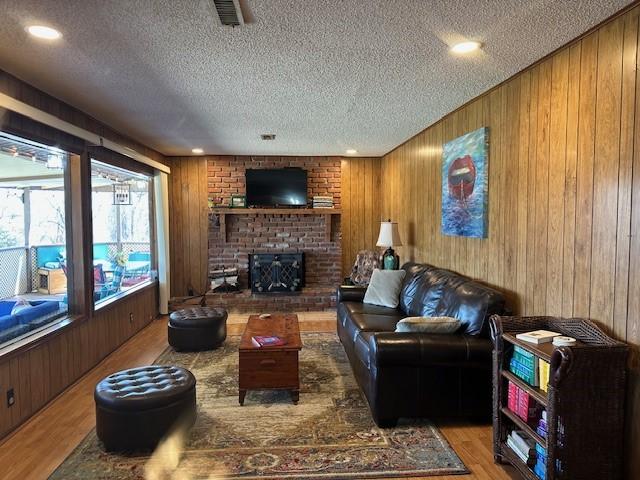 living room featuring wooden walls, wood finished floors, visible vents, a fireplace, and a textured ceiling