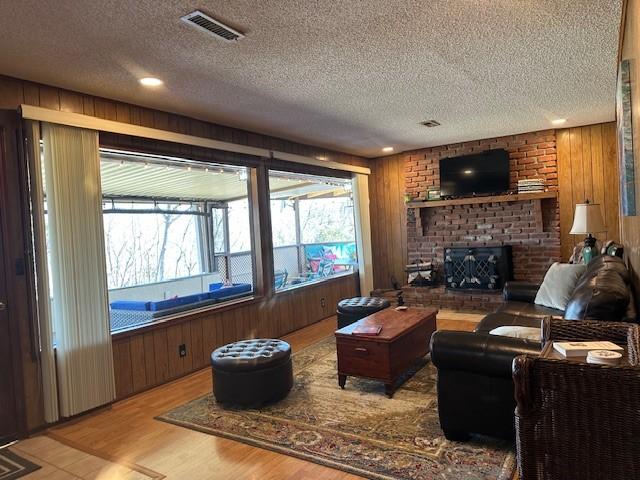 living area featuring visible vents, wooden walls, light wood-type flooring, a fireplace, and a textured ceiling