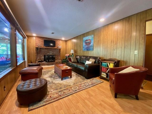 living room with a textured ceiling, a brick fireplace, wood finished floors, and wood walls