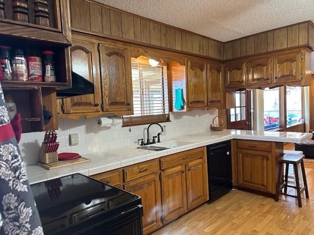 kitchen with brown cabinets, black appliances, a textured ceiling, a peninsula, and light wood finished floors