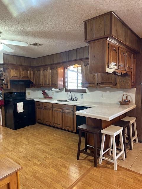 kitchen with light wood finished floors, ceiling fan, a kitchen bar, black electric range, and a sink