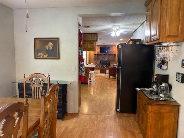 kitchen with a ceiling fan, brown cabinets, freestanding refrigerator, a textured ceiling, and light wood-type flooring