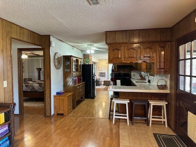 kitchen featuring tile countertops, wooden walls, freestanding refrigerator, ceiling fan, and a sink