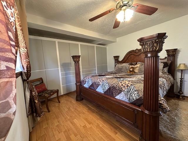 bedroom with ceiling fan, wood finished floors, and a textured ceiling