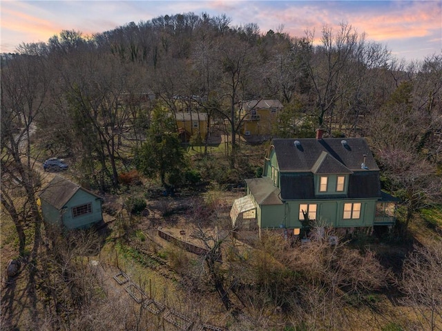 aerial view at dusk featuring a wooded view