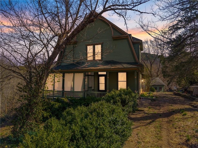 back of property at dusk with a gambrel roof and a porch