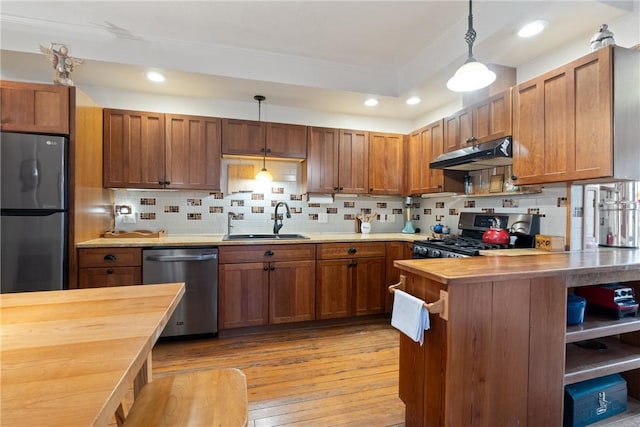 kitchen with a sink, stainless steel appliances, under cabinet range hood, decorative light fixtures, and butcher block counters