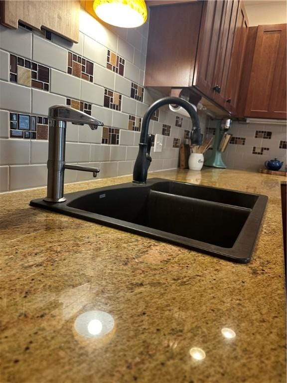 interior details featuring a sink, light stone counters, tasteful backsplash, and brown cabinetry