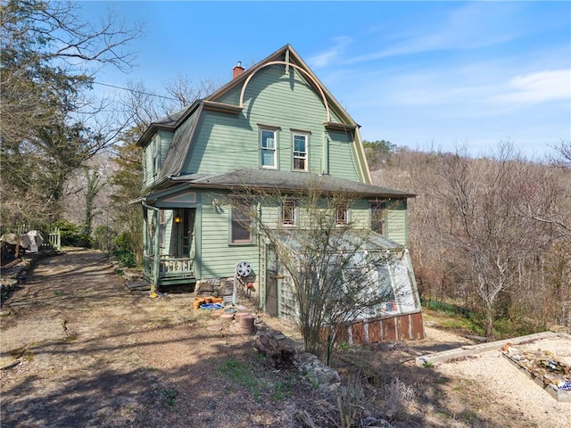 rear view of property featuring a gambrel roof and a chimney