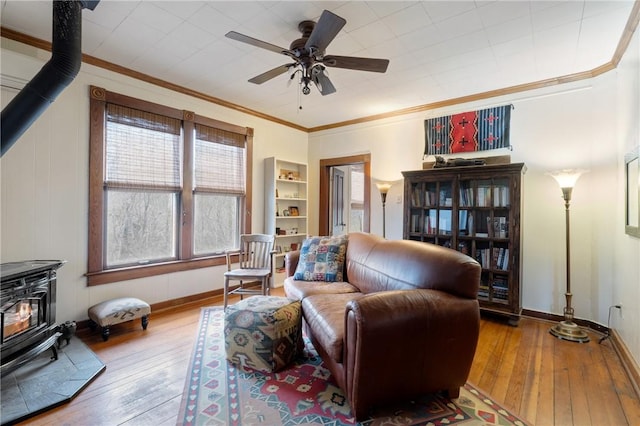 living room featuring wood-type flooring, a ceiling fan, ornamental molding, and a wood stove