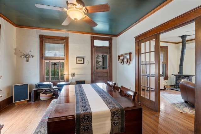 dining area featuring hardwood / wood-style floors, a wood stove, ceiling fan, and ornamental molding