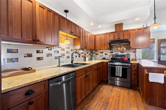 kitchen with backsplash, under cabinet range hood, hardwood / wood-style flooring, stainless steel appliances, and a sink