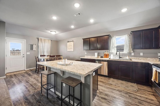 kitchen with a kitchen bar, visible vents, a sink, wood finished floors, and stainless steel appliances