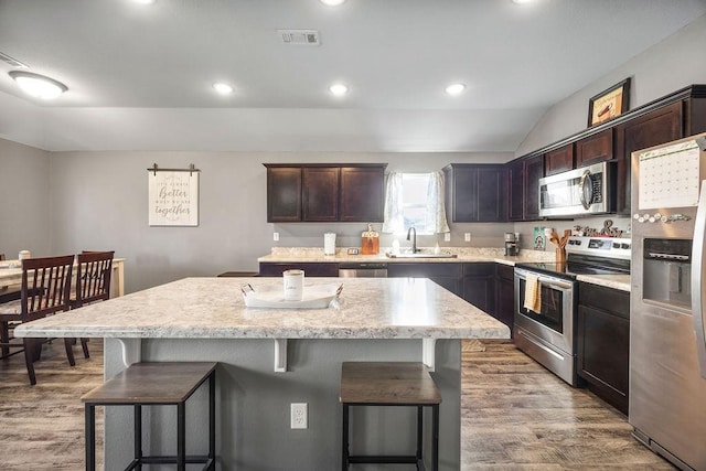 kitchen featuring wood finished floors, a sink, appliances with stainless steel finishes, a kitchen breakfast bar, and a center island