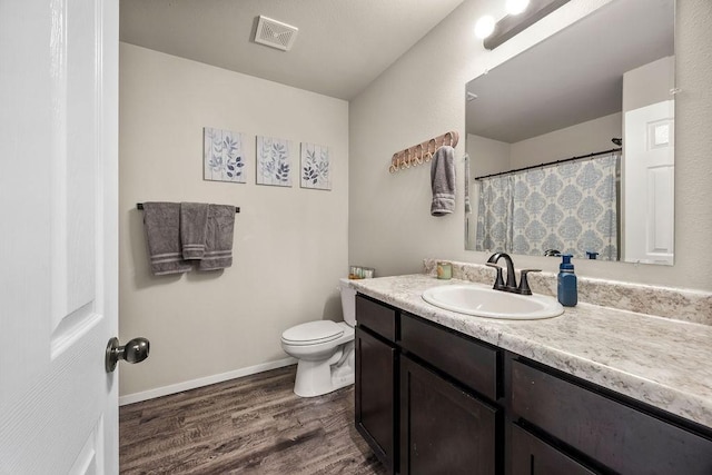 bathroom featuring visible vents, baseboards, toilet, wood finished floors, and vanity