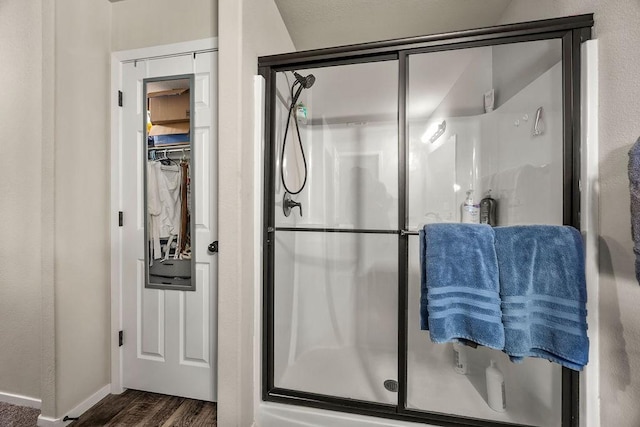 full bath with a spacious closet, a stall shower, baseboards, and wood finished floors