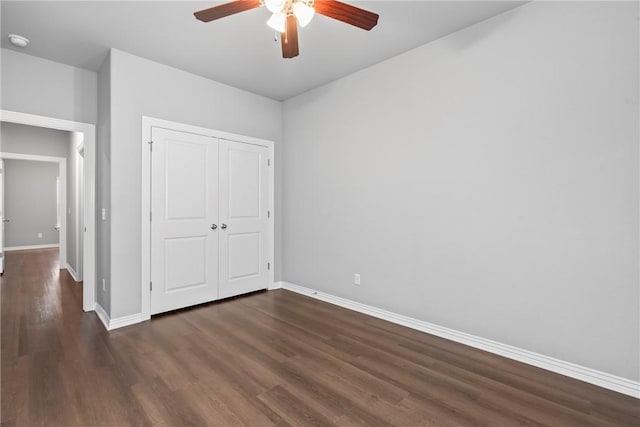 unfurnished bedroom with dark wood-style floors, baseboards, a closet, and ceiling fan