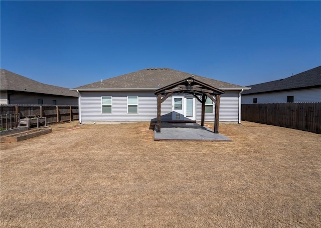 rear view of property with a gazebo, a shingled roof, a fenced backyard, and a patio area