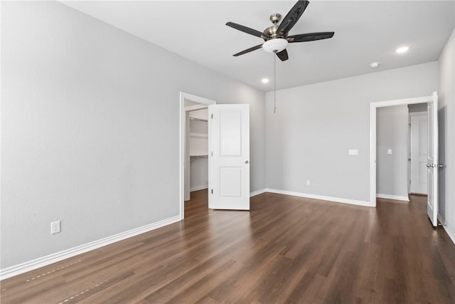 unfurnished bedroom with dark wood finished floors, a spacious closet, a ceiling fan, and baseboards