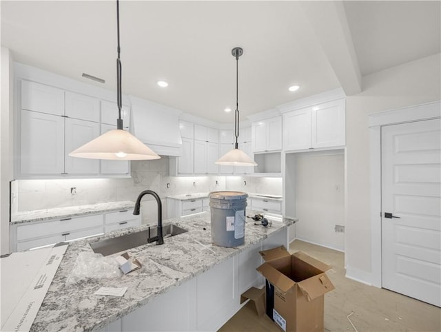 kitchen with pendant lighting, a sink, white cabinets, decorative backsplash, and light stone countertops