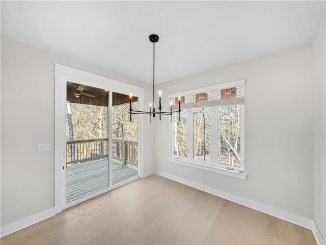 unfurnished dining area with baseboards, a notable chandelier, and wood finished floors