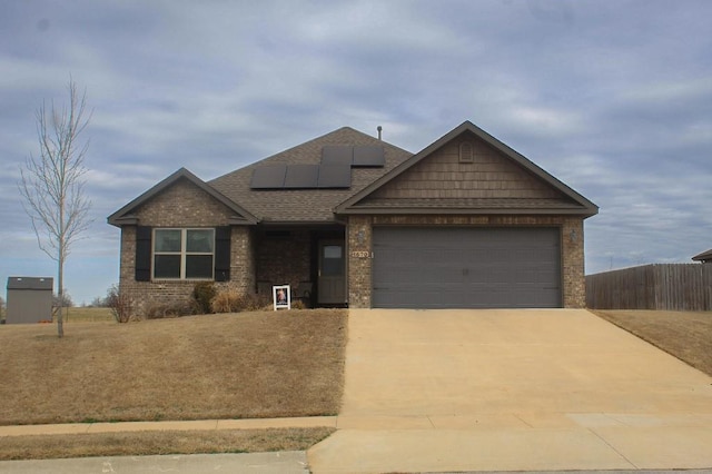 craftsman-style home featuring roof mounted solar panels, fence, roof with shingles, concrete driveway, and an attached garage