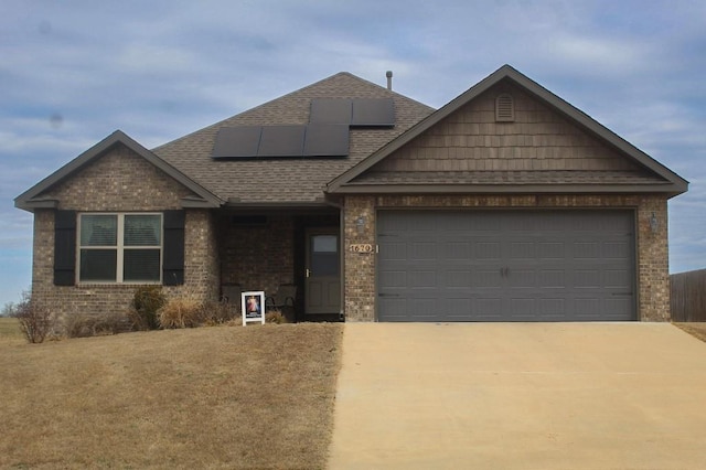 view of front of home with roof with shingles, solar panels, an attached garage, concrete driveway, and brick siding