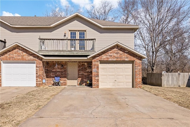 traditional-style house with a balcony, fence, an attached garage, concrete driveway, and brick siding