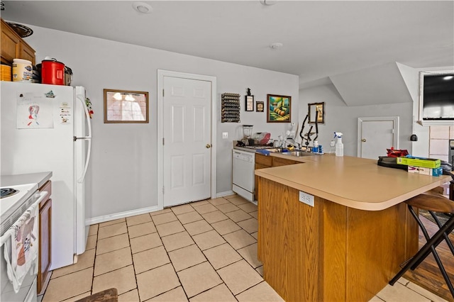 kitchen featuring a kitchen bar, brown cabinets, white appliances, a peninsula, and light countertops