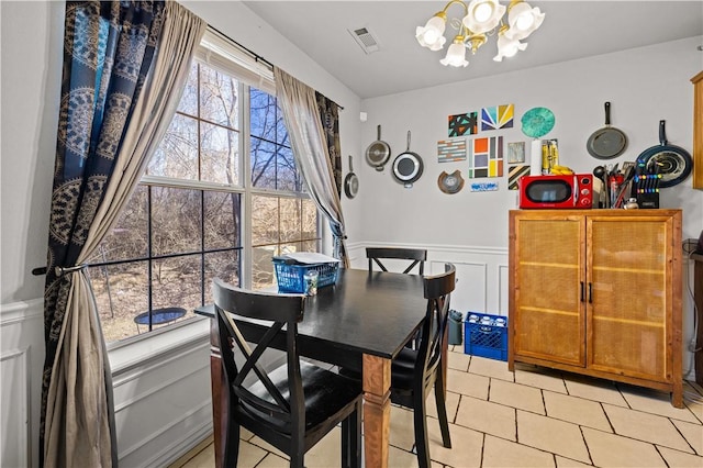 dining space featuring visible vents, a chandelier, light tile patterned floors, wainscoting, and a decorative wall