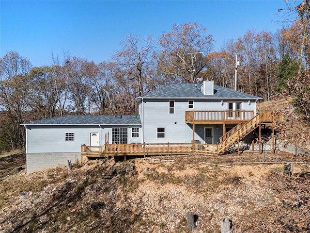 rear view of house featuring stairway, a deck, a chimney, and a shingled roof