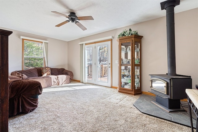 carpeted living room featuring a textured ceiling, a wood stove, baseboards, and ceiling fan