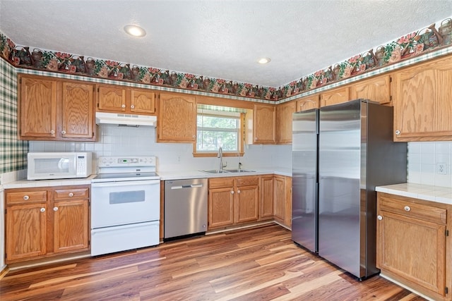 kitchen featuring light wood finished floors, under cabinet range hood, light countertops, stainless steel appliances, and a sink